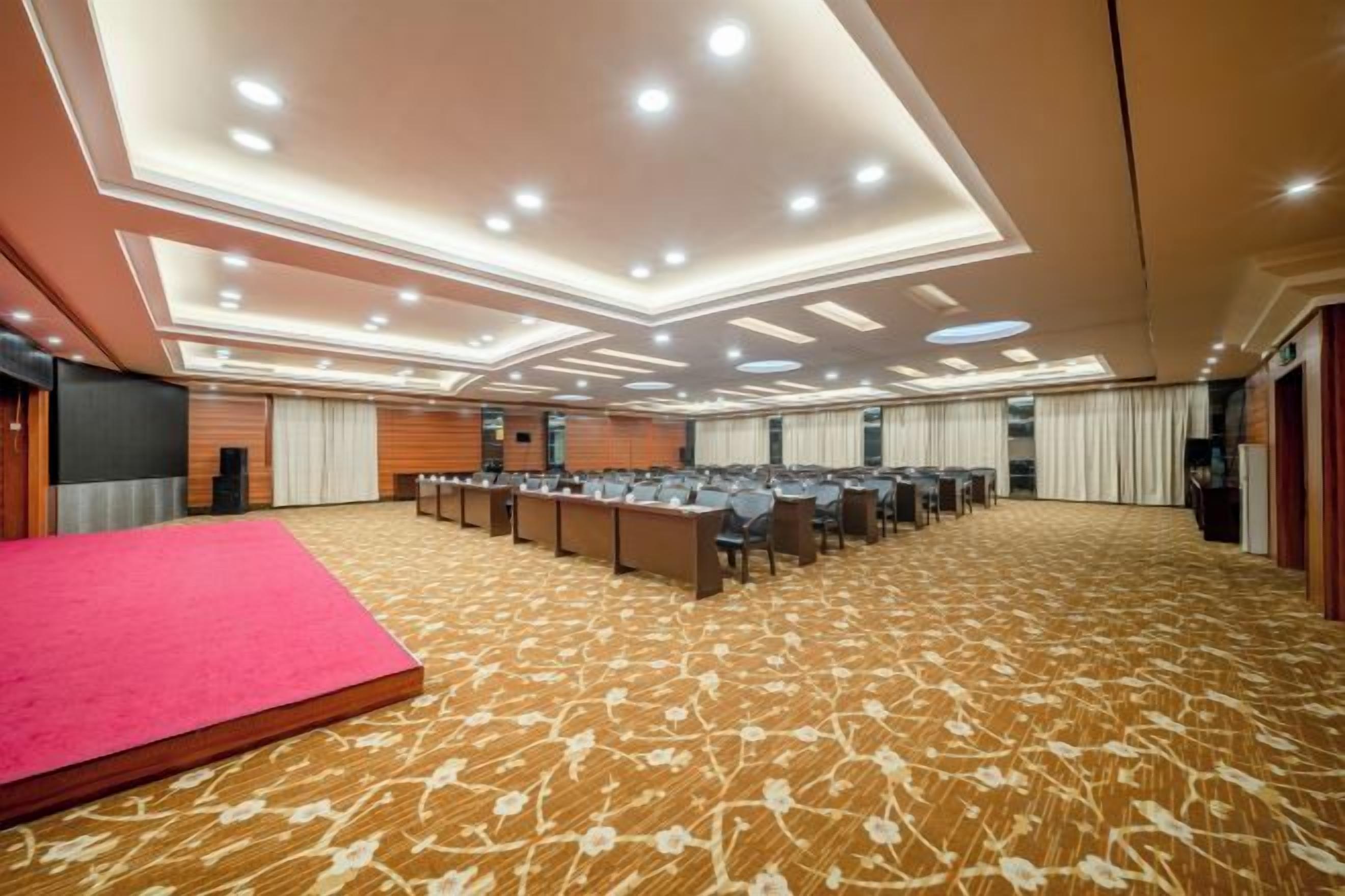 A conference room with a stage, rows of tables, and a carpeted floor.