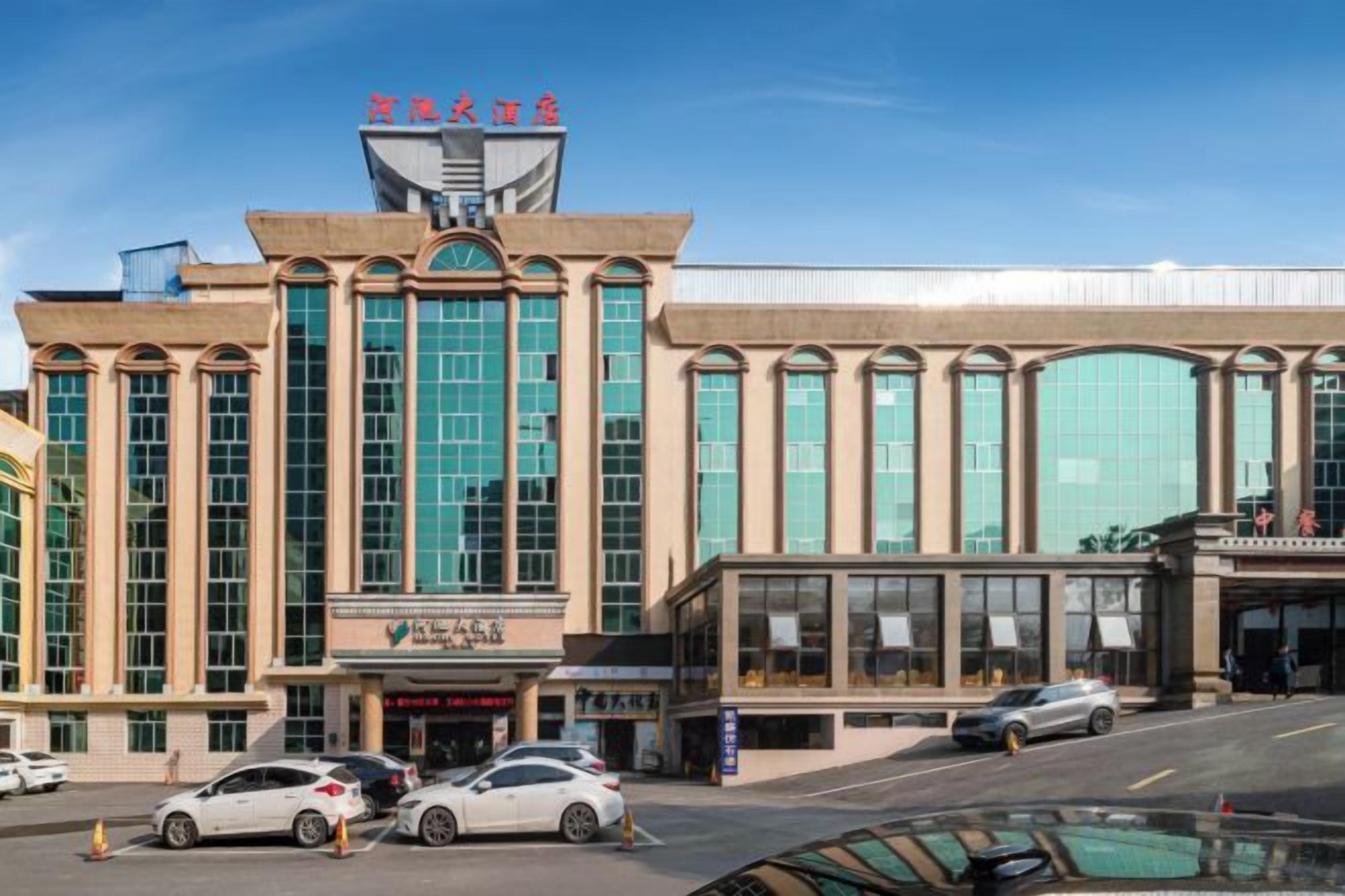A hotel with a large glass facade, a prominent entrance, and a parking lot with several cars.