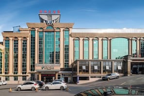 Un hotel con un amplio muro de cristal, una entrada destacada y un estacionamiento con varios coches.