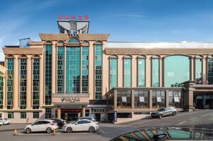 A hotel with a large glass facade, a prominent entrance, and a parking lot with several cars.
