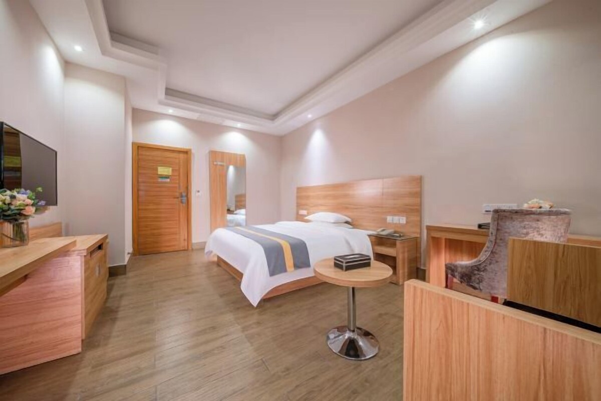 A hotel room with a bed, bedside table, a desk, a chair, and a TV.