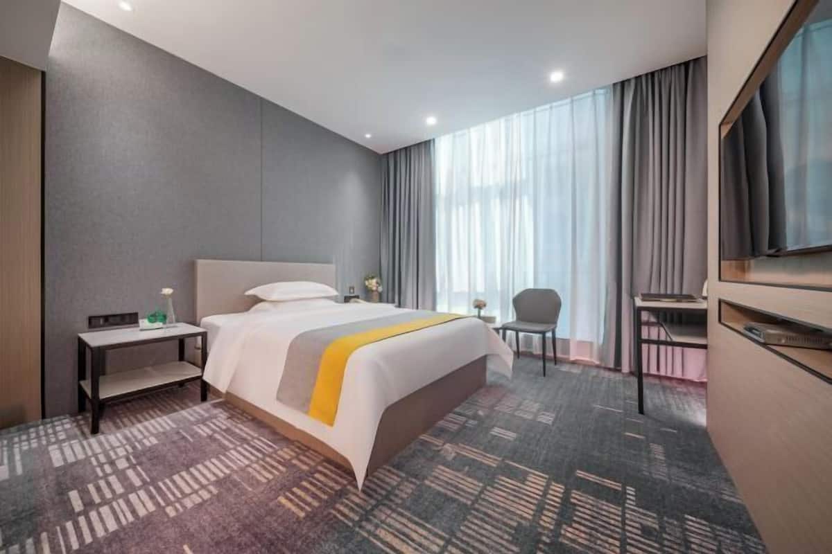 A hotel room with a bed, a desk, a chair, a TV, and a window with curtains.