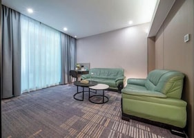Habitación de hotel con un sofá verde, una mesita redonda y un ventanal con cortinas.