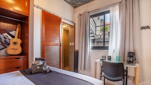 Habitación de hotel con cama, escritorio, silla, guitarra y ventana con cortinas.