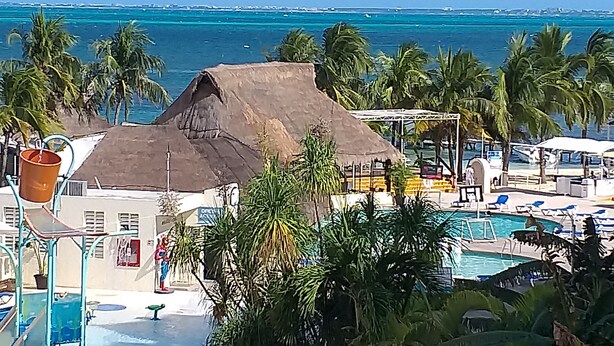 A resort with a pool, palm trees, and a view of the ocean. - Suite Frente AL MAR (Cancún)