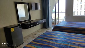 A hotel room with a bed, a desk with a TV, and a small fridge. - Suite Frente AL MAR (Cancún)