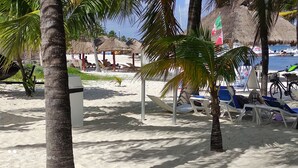 A beach with thatched-roof huts, palm trees, and beach chairs. - Suite Frente AL MAR (Cancún)