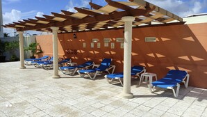 A covered outdoor seating area with blue lounge chairs and a pergola structure. - Suite Frente AL MAR (Cancún)