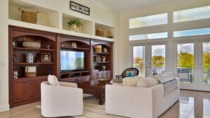 A spacious living room with a large flat-screen TV, two white sofas, a wooden entertainment center, and a large sliding glass door leading to an outdoor patio. - Riverview Paradise, Sleeps 18, River, Pool/Spa, kayaks  (Alva)