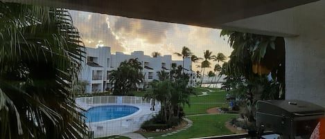 A view of a pool surrounded by palm trees and a building with multiple balconies.