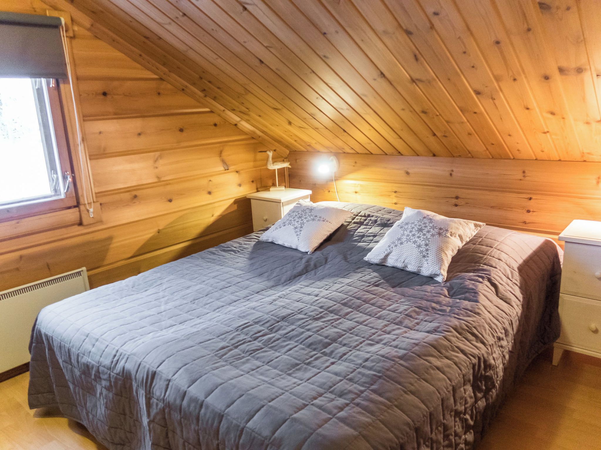 Ett sovrum i en stuga med träpanel, inrett med en säng, ett nattduksbord, en lampa och ett fönster.