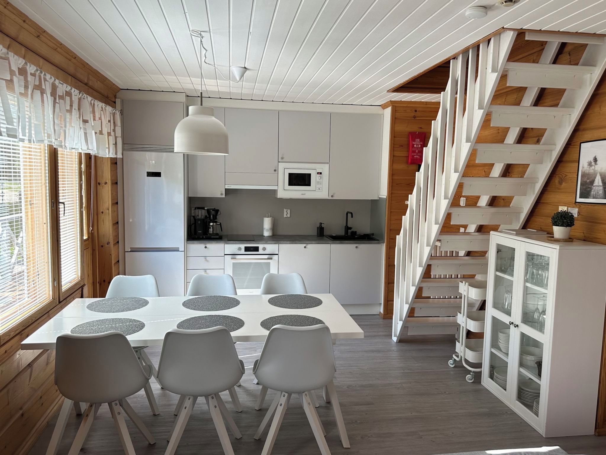 Een moderne keuken met witte kasten, een eettafel met stoelen en een trap met houten balustrade.