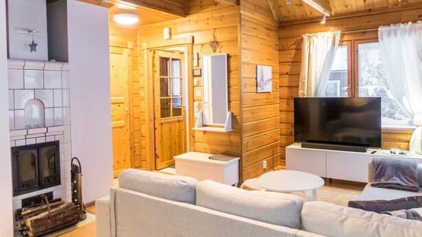 Interior acogedor de una cabaña de madera con chimenea, un sofá, un televisor y una ventana con cortinas.