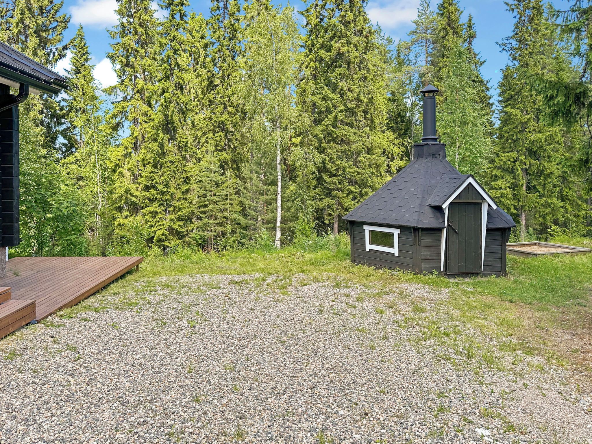 Eine kleine Holzhütte mit Schornstein, umgeben von Kies und dichtem Wald.