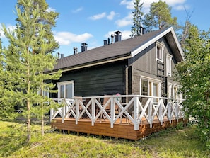 Une cabane dotée d’une terrasse en bois et d’une balustrade blanche, entourée d’arbres.