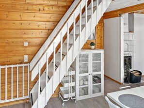 Un intérieur en bois avec un escalier blanc, un meuble avec des portes en verre et un coin repas.