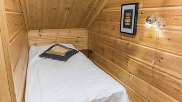 A wooden cabin room with a bed, a framed sign on the wall, and a small stool.