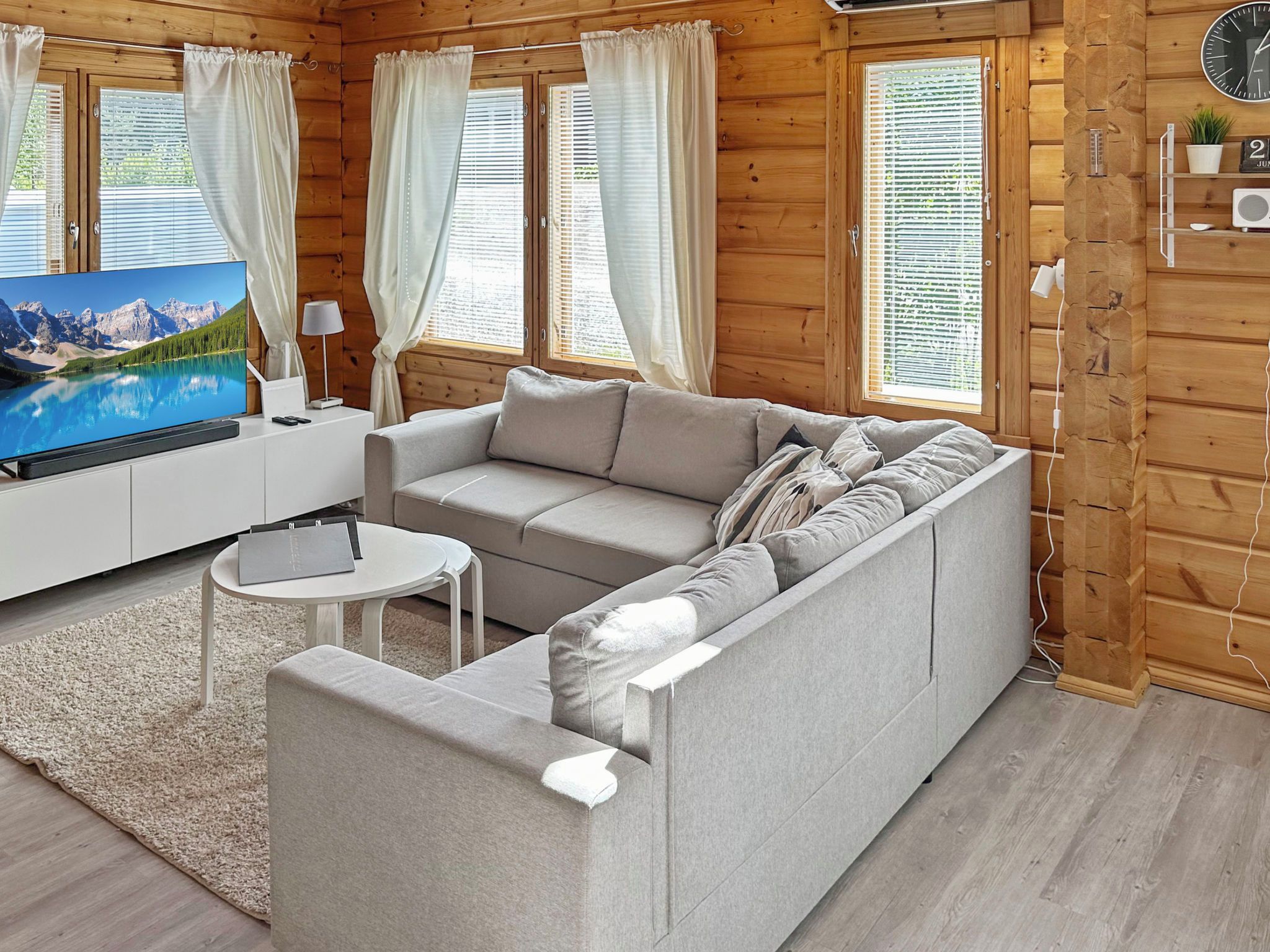 Interior moderno de uma cabana de toras com sofá, televisão e uma pequena mesa.