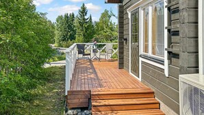 Una terraza de madera con mobiliario exterior, un borde de piedra y vista a un área boscosa.