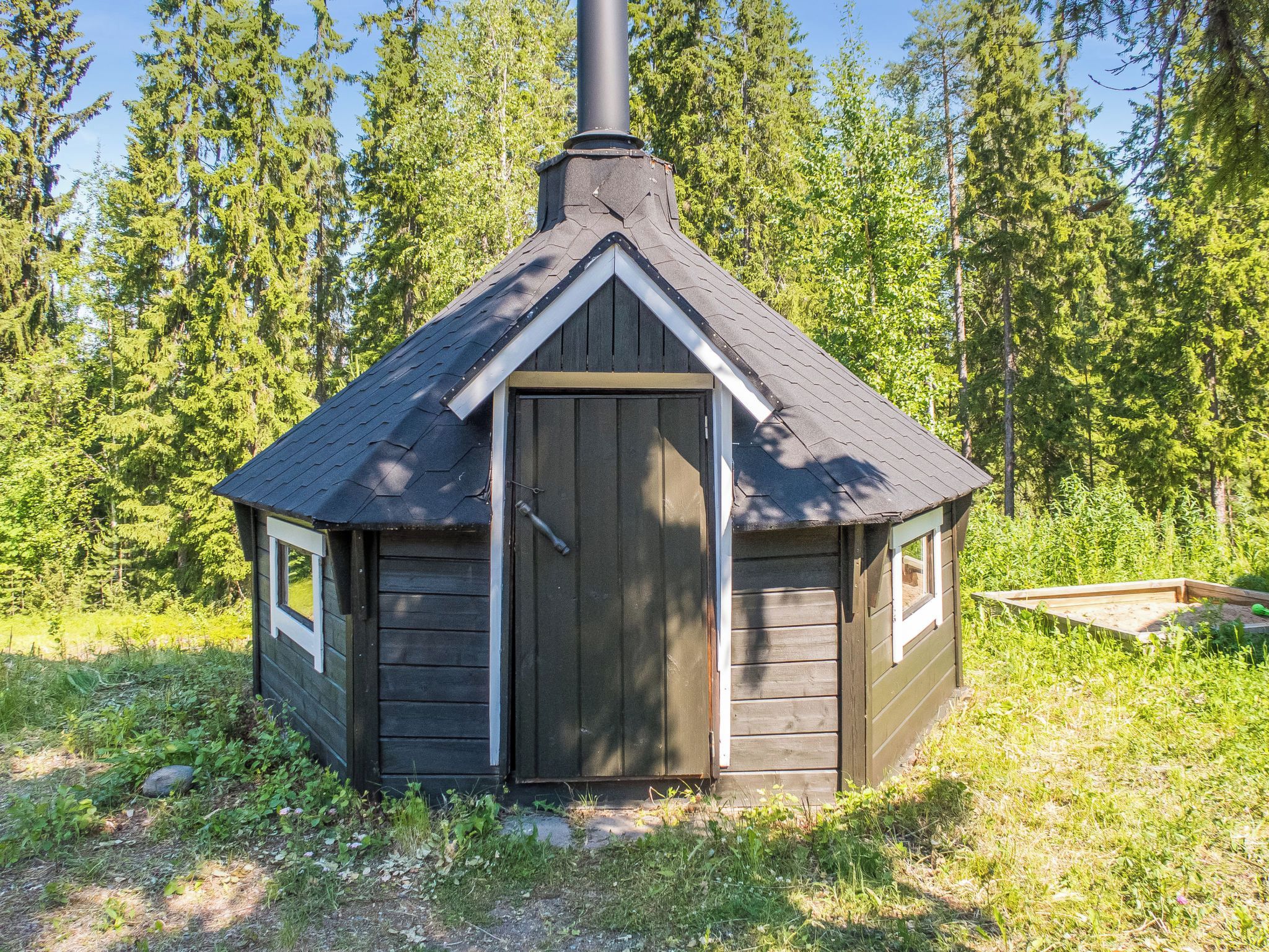 A small wooden cabin with a gabled roof and a chimney, surrounded by trees.