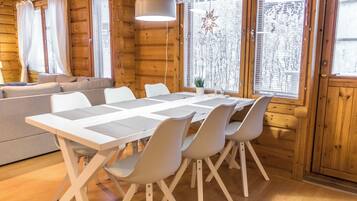 A wooden cabin interior with a dining table, chairs, a sofa, and a hanging light fixture.
