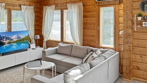 Interior acogedor de una cabaña de madera con un sofá seccional, un televisor de pantalla plana y una pequeña mesa redonda.