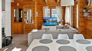 Un interior moderno de cabaña de troncos con comedor, sala de estar con televisor y cocina.