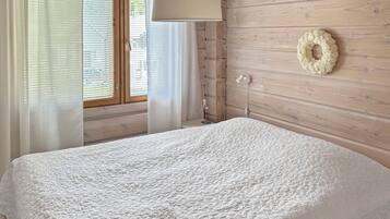 Quarto com cama, janela com persianas, luminária na parede e um arranjo decorativo.