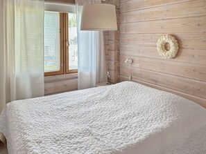A bedroom with a bed, a window with blinds, a wall-mounted lamp, and a decorative wreath.