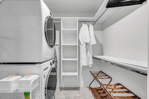 A laundry room with a washing machine, drying rack, and shelves for hanging clothes.