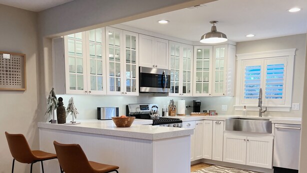 A modern kitchen with white cabinetry, a large island with bar stools, a stainless steel sink, and a microwave.