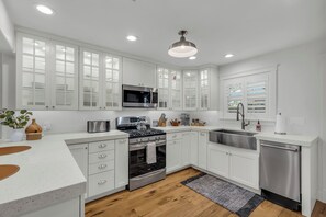 A modern kitchen with white cabinetry, stainless steel appliances, and a wooden floor.