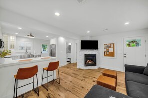 Een moderne keuken met een centraal eiland, een eethoek met twee stoelen, een open haard en een woonkamer met een bank en voetenbankje.