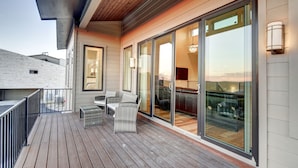 Una terraza de madera con mobiliario exterior, grandes puertas correderas de vidrio que dan a una zona de cocina y un diseño exterior moderno.