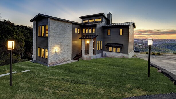 Una casa moderna de dos pisos con fachada de piedra, ventanas amplias y un césped bien cuidado.