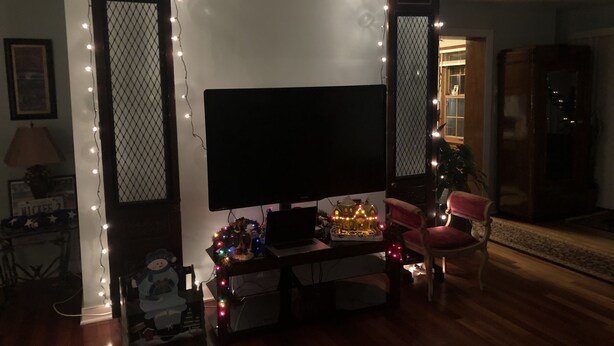 Una sala de estar con televisor, una mesita con un árbol de Navidad y una silla.