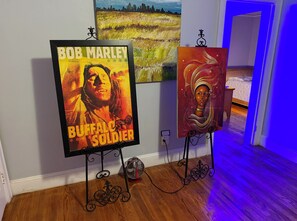 Artwork on easels in a room with wooden flooring and a bed in the background. - The Raleigh Den/ Sleeps 8/ Walk to Iron Works & Ritz (Raleigh)