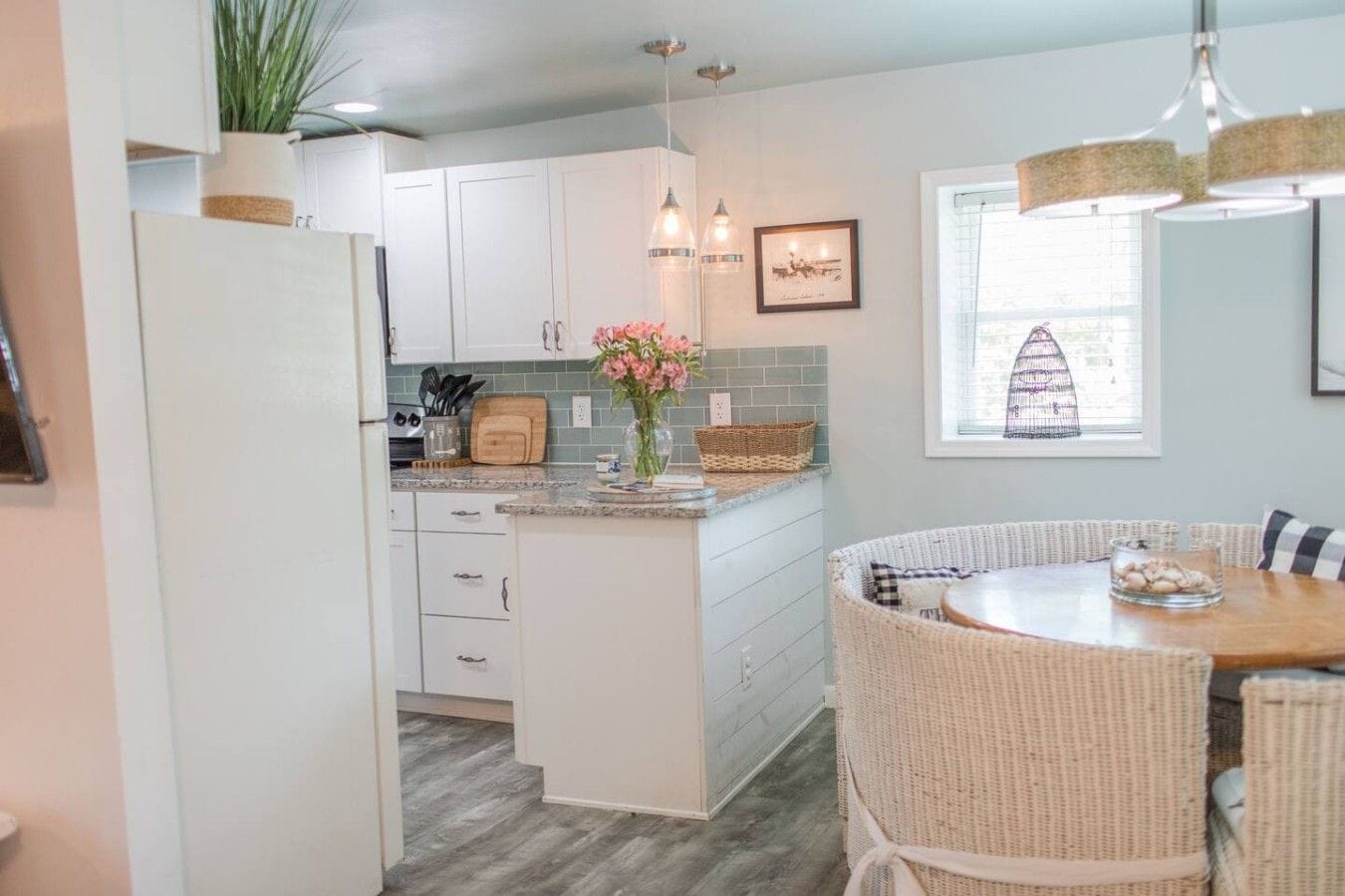 A kitchen with white cabinets, a central island, wicker chairs, and a dining table.