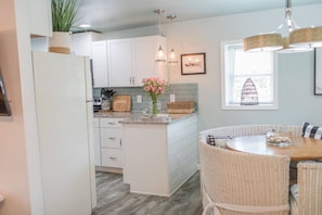 A kitchen with white cabinets, a central island, wicker chairs, and a dining table.
