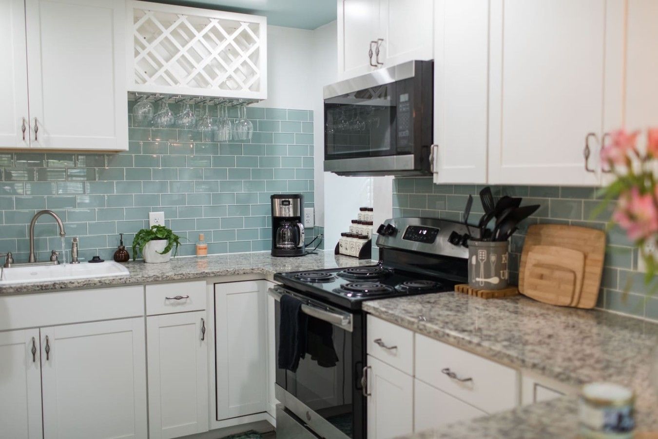 A kitchen with white cabinets, a black microwave, a stove, and a coffee maker.