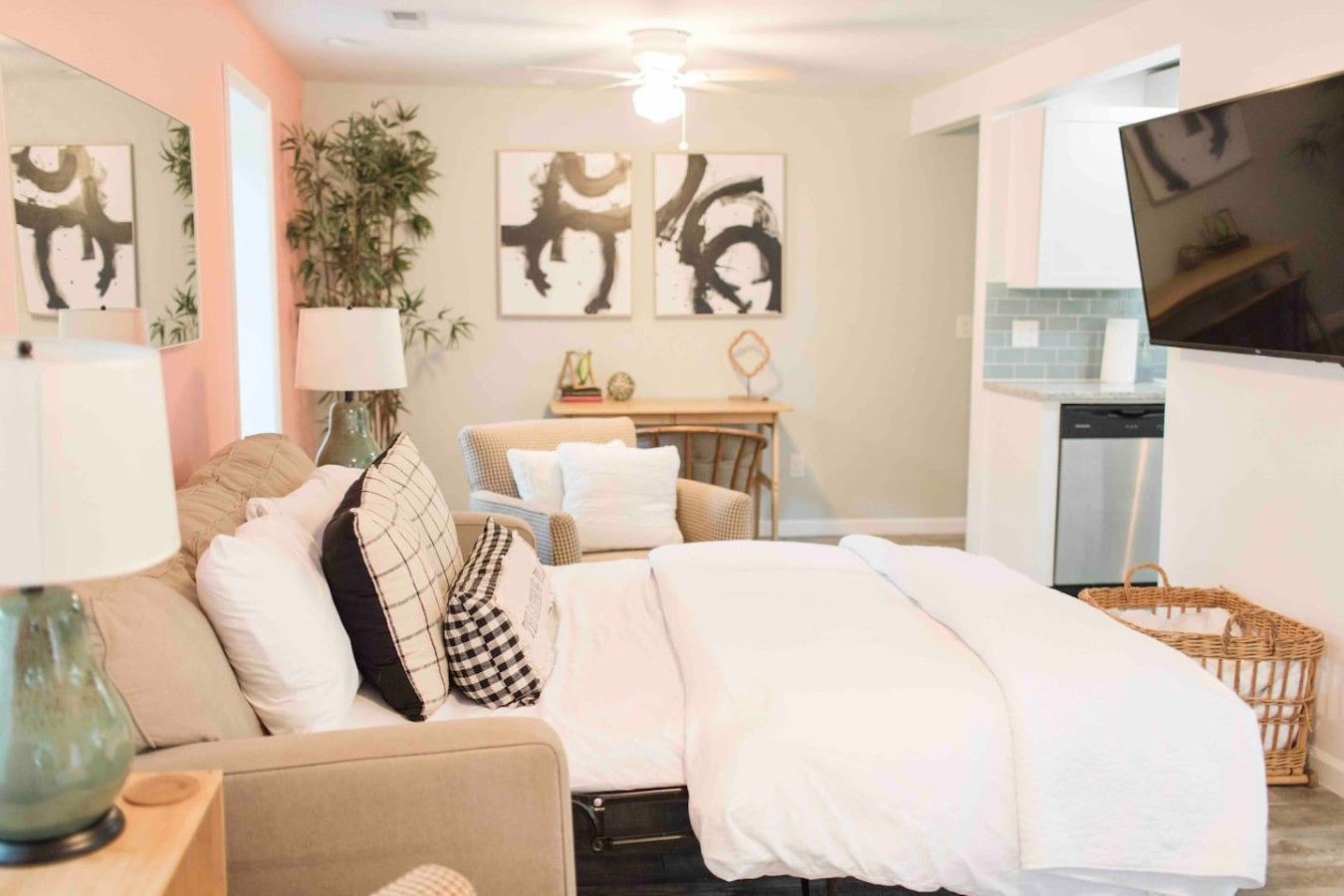 A hotel room with a bed, a sofa, a desk, a television, and artwork on the walls.