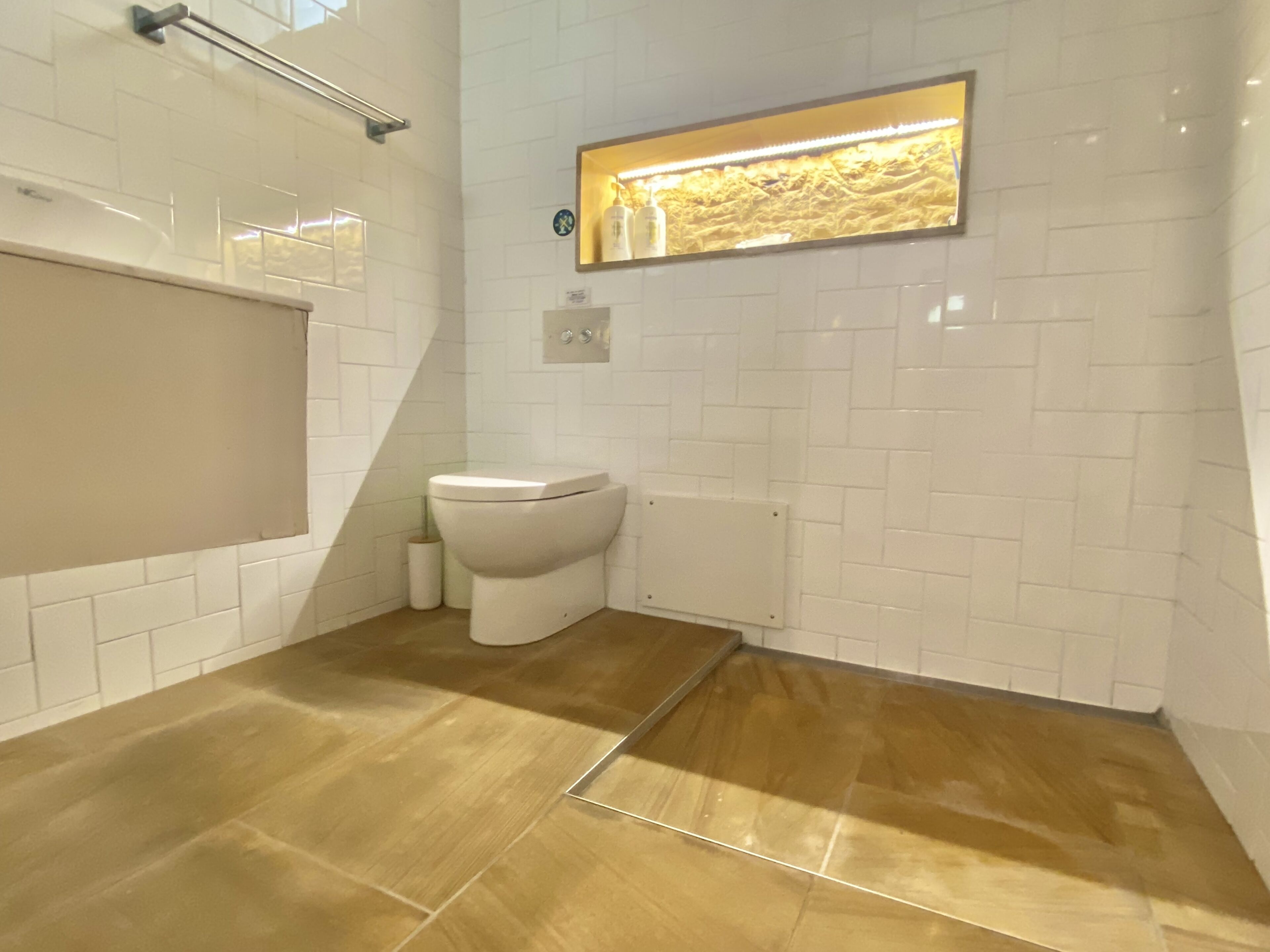 A bathroom with white subway tiles, a toilet, a towel rack, and a wooden floor.