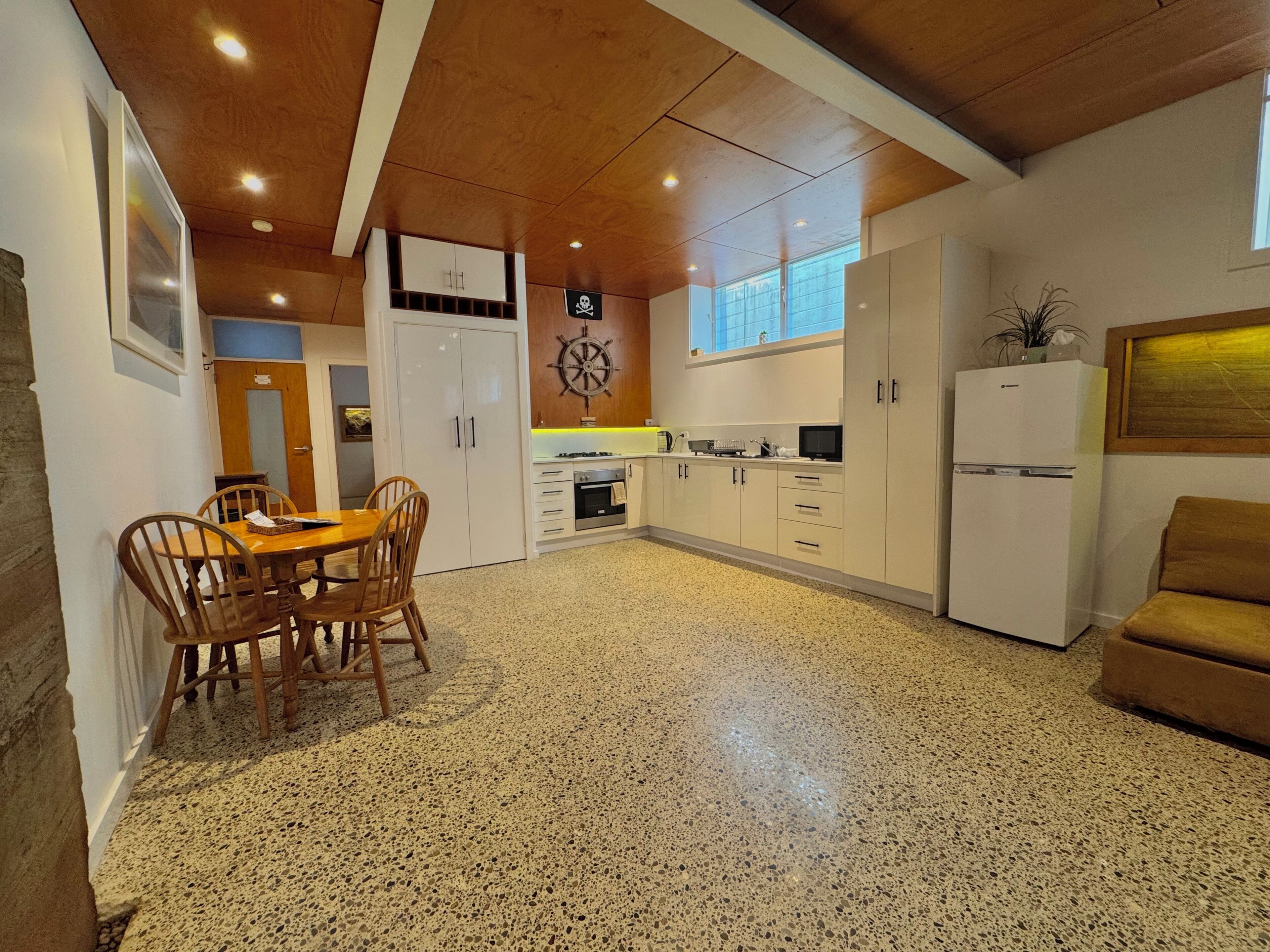 Een keuken met een eettafel en stoelen, een koelkast, en een klok aan de muur.