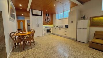 Een keuken met een eettafel en stoelen, een koelkast, en een klok aan de muur.