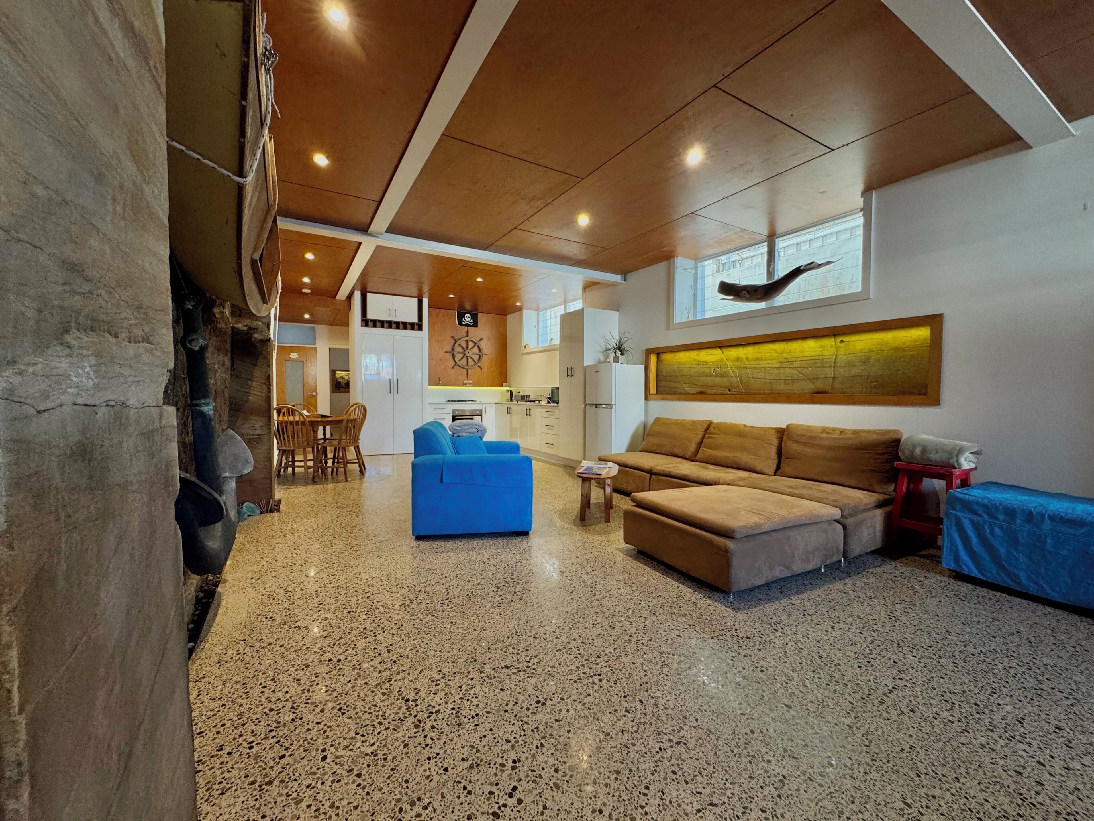 A spacious living area with a kitchen in the background, a blue sofa, a brown sofa, and a small table.