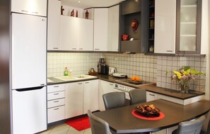 A modern kitchen with white cabinets, a built-in oven, a coffee maker, and a dining table with chairs.