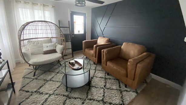 Un salon doté d’un ventilateur de plafond, d’un fauteuil rond en osier avec un coussin, d’un canapé en cuir marron et d’une table basse avec un plateau.