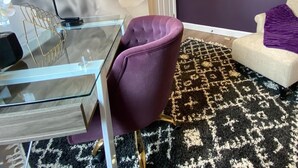 Un salon moderne avec une table basse en verre, un fauteuil violet, un tapis à motifs et un mur orné d’un grand motif floral.