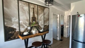 Une cuisine moderne agrémentée d’un grand tableau représentant la Tour Eiffel, d’un réfrigérateur en acier inoxydable et de deux tabourets noirs.