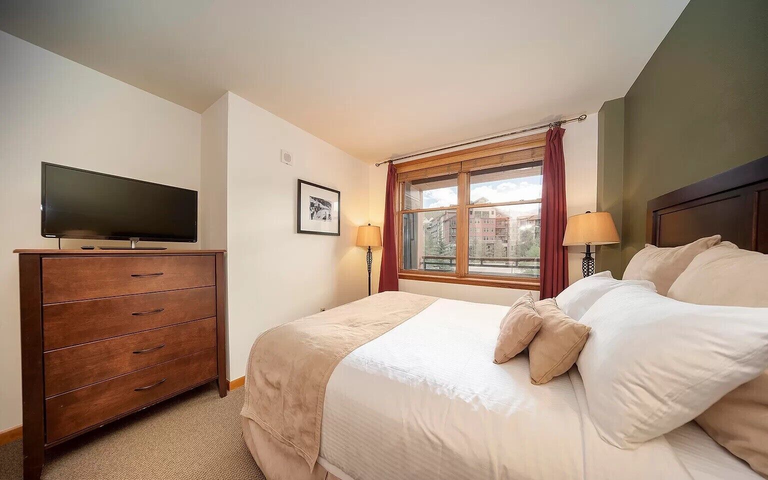 A hotel room with a bed, a dresser, a TV, a window with curtains, and a lamp.